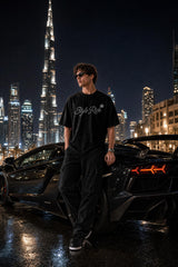 Modelo con la playera Style Rich de noche en Dubái junto a un superdeportivo negro